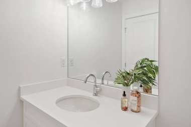 Banyo lavabosu, üzerinde ayna ve tezgahın üzerinde bir şişe losyonla. Lavabo beyaz ve ayna temiz.