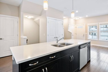 Beyaz tezgahı ve siyah dolapları olan bir mutfak. Lavabo gümüş, bulaşık makinesi gümüş.