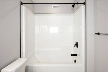 Siyah duş perdesi ve beyaz tuvaleti olan beyaz bir banyo. Duş boş ve tuvalet kapalı.