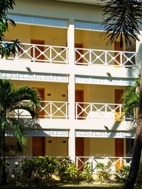 Arka planda balkonları ve palmiye ağaçları olan beyaz binalar. Binalar uzun ve modern bir tasarıma sahip.