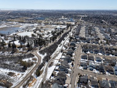 Evleri ve yolları olan karlı bir şehir manzarası. Evlerin çoğu beyaz ve yol karla kaplı. Sahne huzurlu ve sakin, kar zemini kaplıyor.