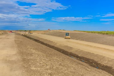 İnşaat alanında ön planda büyük bir ekipman var. Gökyüzü mavi ve birkaç bulut var.