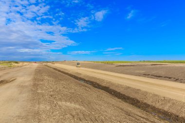Yol kuru ve tozlu bir alana inşa ediliyor. Gökyüzü açık ve mavi ve görünürde hiç bulut yok.