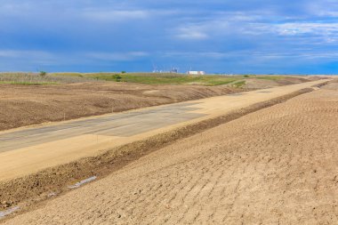 Yan tarafında çit olan kirli bir yol. Yol boş ve gökyüzü bulutlu.