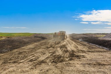 Kamyon toprak bir yolda ilerliyor. Gökyüzü mavi ve hiç bulut yok. Yol çamurlu ve kamyon tozlanıyor.