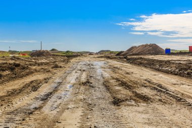 Arka planda mavi bir çöp konteynırı olan kirli bir yol. Yol çamurlu ve üzerinde bir sürü pislik var.