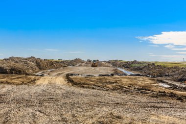 Üzerinde büyük bir kamyon olan kirli bir yol. Yol boş ve gökyüzü mavi.
