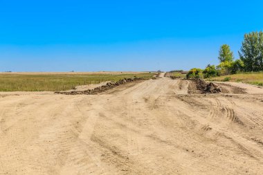 Arka planda mavi gökyüzü olan kirli bir yol. Yol boş ve üzerinde ne insan ne de araç var.