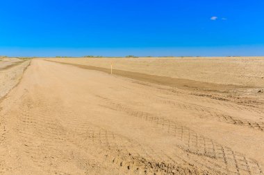 Arka planda mavi gökyüzü olan kuru, tozlu bir yol. Yol boş ve etrafta kimse yok.