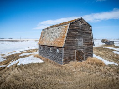 Büyük, eski ahır bir kar tarlasında duruyor. Ahır çimlerle çevrili ve gökyüzü temiz.