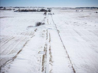 Bir tarlanın ortasında, karlı, boş bir yol. Yol uzun ve düz, ve etrafta ne araba ne de insan var. Kar derin ve zemini kaplıyor, manzarayı huzurlu kılıyor.