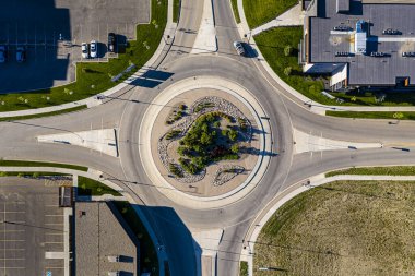 Ortasında büyük bir ağaç olan yuvarlak bir kavşağın görüntüsü. Kavşak binalar ve arabalarla çevrili.