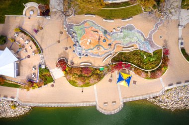 Büyük bir çeşmesi ve gitar heykeli olan bir park. Çeşmenin etrafında banklar ve masalar var.