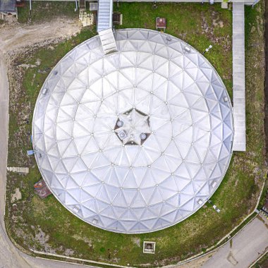 Büyük, yuvarlak, gümüş kubbe yukarıdan görülüyor. Kubbe çimlerle çevrilidir ve daha büyük bir yapının parçasıdır. İhtişam ve önem kavramı