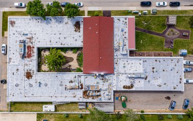 Kırmızı çatılı ve önünde yeşil ağaç olan beyaz bir bina. Çatı enkazla kaplı ve bina terk edilmiş gibi görünüyor.