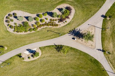 Üç bölüme ayrılmış bir patika ile park et. Yol ağaçlar ve otlarla çevrili.