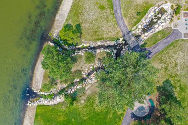 Taş duvarın ortasında büyük bir ağaçla park et. Ağaç yemyeşil çimenlik bir alanla çevrili ve yakınlarda bir su kütlesi var. Kaya duvarı parkın önemli bir özelliğidir.