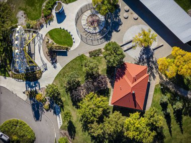 Çocuk parkı ve çatısı olan kırmızı bir bina. Park ağaçlar ve otlarla dolu.