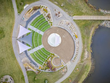 Sahnesi ve göleti olan büyük yeşil bir park. Sahne çimenler ve ağaçlarla çevrili.