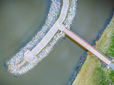 Kayalık bir kıyı şeridi olan bir su kütlesinin üzerinde köprü. Köprü ahşap ve su boyunca uzanıyor.