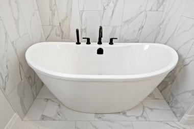 Siyah musluğu ve siyah sapı olan beyaz bir küvet. Küvet beyaz fayanslarla dolu bir banyoda.