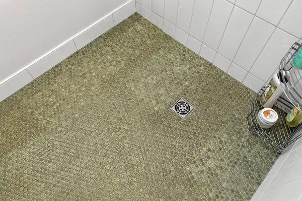 Yeşil döşemeli ve beyaz duvarlı banyo. Zeminin ortasında bir duş gideri görünür.