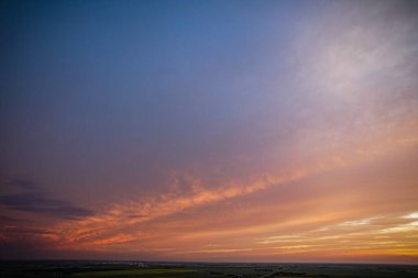 Mavi gökyüzü ve birkaç bulutla güzel bir günbatımı. Gökyüzü ılık turuncu bir tonla doludur. Huzurlu ve huzurlu bir atmosfer yaratır.