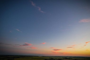 Gökyüzünde birkaç bulut olan bir tarlanın üzerinde güzel bir günbatımı. Gökyüzü pembemsi bir tonu olan koyu mavi bir renktir.
