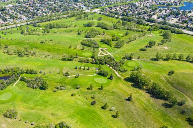 Yeşil çimenli çayırları ve ağaçları olan golf sahası. Golf sahası evler ve göl ile çevrili.