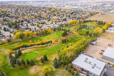 Yeşil çimenli bir alanı ve göleti olan golf sahası. Golf sahası evler ve binalarla çevrili.