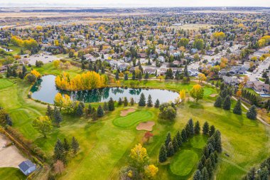 Arka planda ağaçlar ve gölcüklü golf sahası. Gölet yeşil, ağaçlar sarı.