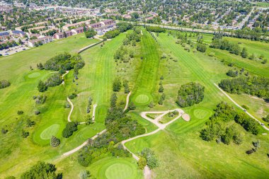 Yeşil çimenli bir tarlası ve birkaç ağacı olan golf sahası. Golf sahası yerleşim bölgesinde.