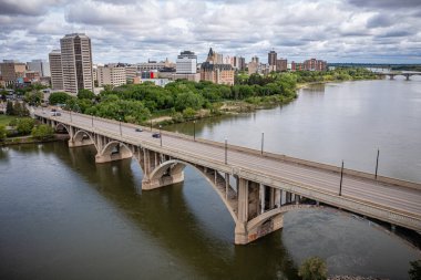 Köprü, bir şehirde bir nehri kapsar. Köprü yüksek binalar ve ağaçlarla çevrilidir. Su sakin ve gökyüzü bulutlu.