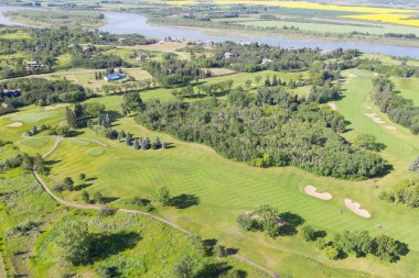 Arka planda nehir olan golf sahası. Golf sahası ağaçlarla çevrili ve yeşil çimenli bir alanı var.