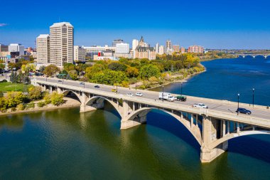 Köprü, arka planda bir şehir bulunan bir nehri kapsar. Köprü, üzerinde yeşil bir kamyonun geçtiği büyük, beyaz bir yapıdır. Şehir hareketlilikle, arabalarla dolup taşıyor.