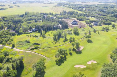 Yeşil çimenli bir tarlası ve arka planda ağaçları olan golf sahası. Golf sahası toprak bir yol ile çevrili.