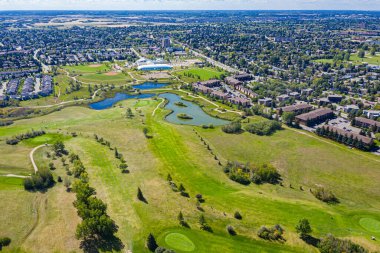 Göllü golf sahası ve arka planda birkaç ev. Golf sahası ağaçlar ve otlarla çevrili.