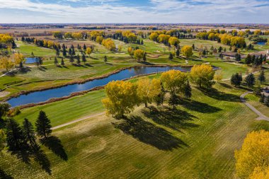Arka planda göl olan golf sahası. Ağaçlar sarı ve kahverengidir.