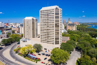 Üzerinde kırmızı işaret olan büyük bir bina. Bina ağaçlar ve arabalarla çevrili. Gökyüzü mavi ve güneş parlıyor.