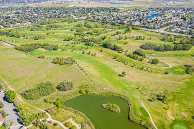 Ortasında gölet olan golf sahası. Gölet ağaçlar ve otlarla çevrilidir. Golf sahası yerleşim bölgesinde.