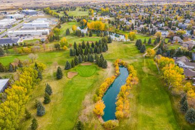 Arka planda ağaçlar ve gölcüklü golf sahası. Gölet ağaçlarla çevrilidir ve golf sahası yerleşim bölgesinde yer almaktadır.