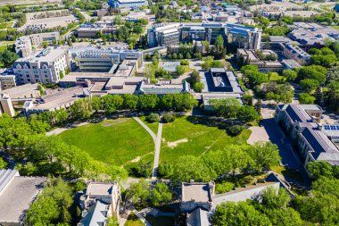 Merkezinde büyük yeşil bir alan olan bir üniversite kampüsü manzarası. Binaların çoğu tuğladan ve etrafa saçılmış birkaç ağaç var.