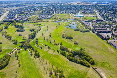 Yeşil tarlası ve göleti olan golf sahası. Golf sahası evler ve binalarla çevrili.