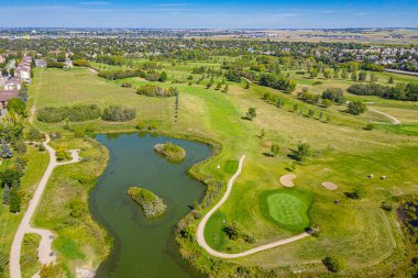 Ortasında gölet olan golf sahası. Gölet ağaçlar ve otlarla çevrilidir. Golf sahası yerleşim bölgesinde.