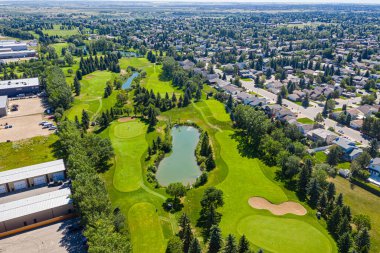 Ortasında gölet olan golf sahası. Gölet ağaçlar ve otlarla çevrilidir. Golf sahası yerleşim bölgesinde.