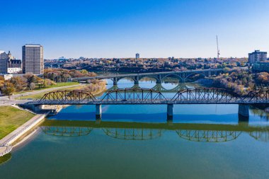 Köprü, arka planda bir şehir bulunan bir nehri kapsar. Köprü, şehrin ve aşağıdaki suyun bir yansımasıdır.
