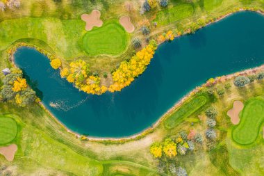 İçinden mavi bir su yolu geçen golf sahası. Su yolu ağaçlar ve otlarla çevrili.