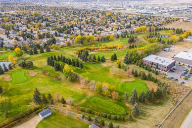 Yeşil çimenli bir tarlası ve arka planda ağaçları olan golf sahası. Golf sahası evler ve binalarla çevrili.