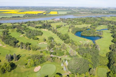 Arka planda göl olan golf sahası. Golf sahası ağaçlarla çevrili ve yeşil çimenli bir alanı var.