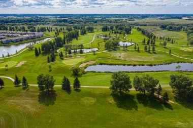 Arka planda göl olan golf sahası. Golf sahası ağaçlar ve evlerle çevrili.
